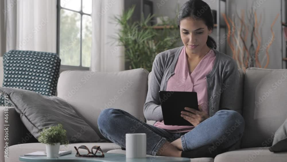 young arab woman sits on the sofa using tablet computer,mixed race brunette girl holding touchscreen device browsing internet onilne swipe screen indoors at home