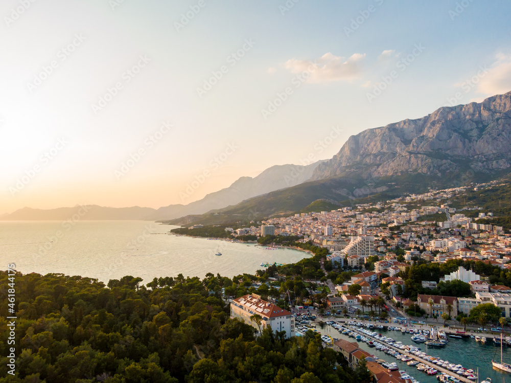 Drone aerial view of Makarska city, Croatia. Sunset over the city, beach and se. Biokovo mountains in the background. Summer time.