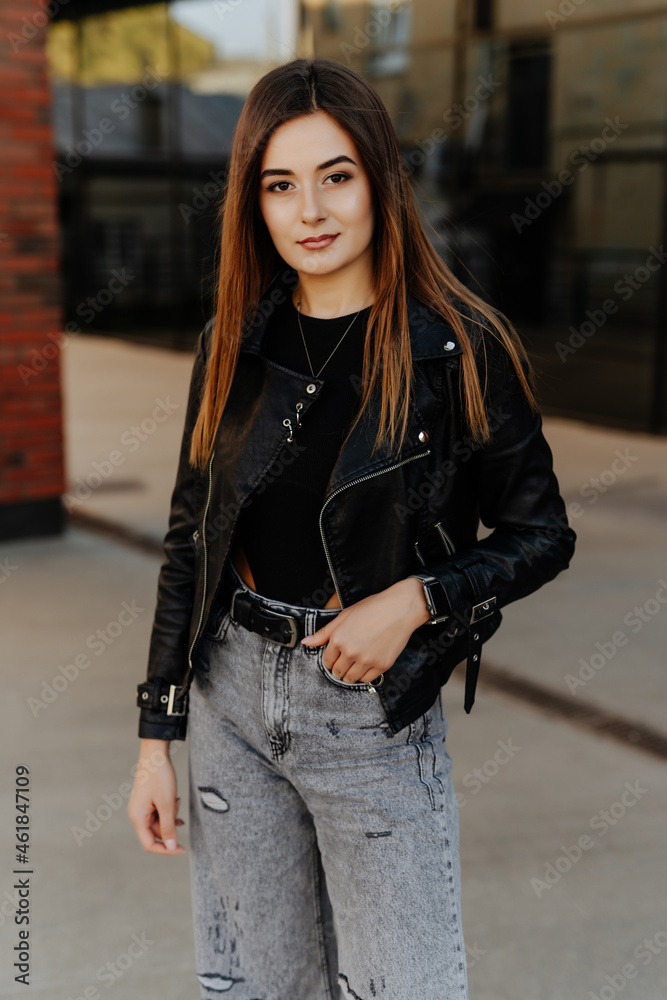 Beautiful young woman in black leather jacket posing on the street