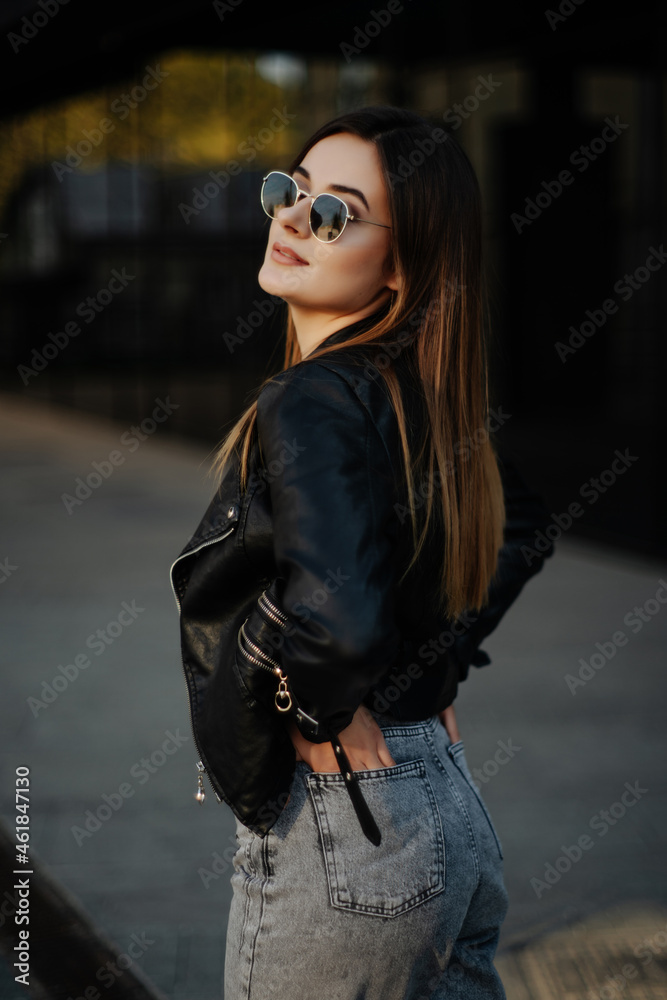 Young woman in sunglasses and black leather jacket posing outdoor