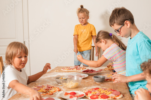 Happy kids sit at a table in the kitchen and make pizza
