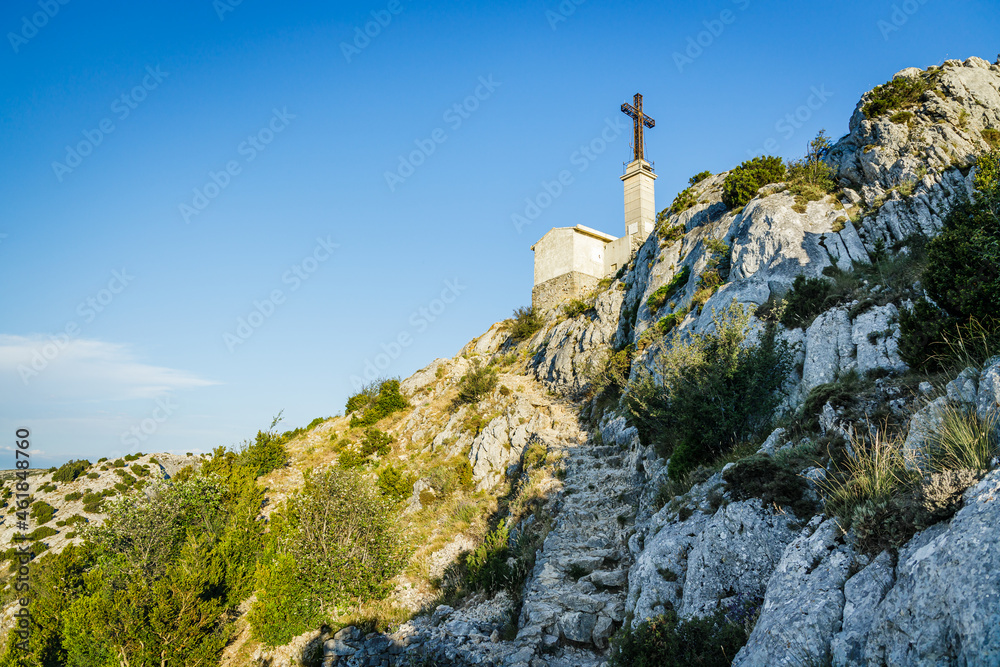 View of the Croix de Provence cross, and the top of Montagne Sainte-Victoire mountain from the northern rocky trail of the Sainte-Victoire Priory in Provence, France