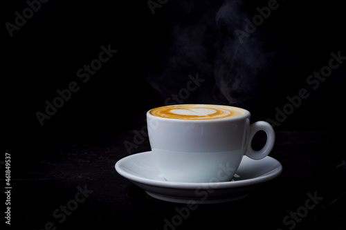 Cappuccino with steam in white cup on the black background