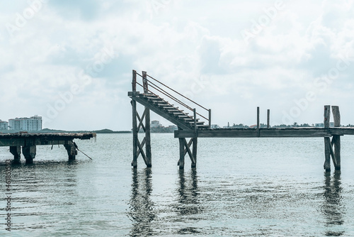 Abandoned and damaged wooden jetty bridge with staircase over sea water surface against cloudy sky © Aerial Film Studio