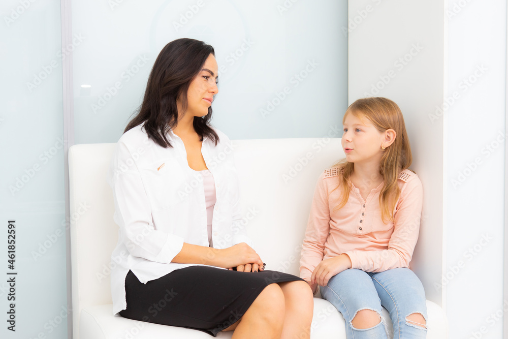 A female doctor with a little girl sitting on a couch in a clinic.