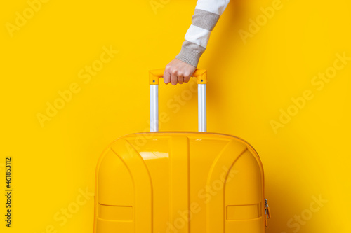Fototapeta Female hand holds a yellow suitcase on a bright yellow background