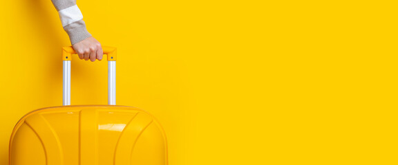 Female hand holds a yellow suitcase on a bright yellow background. Banner