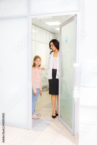 A beautiful woman opens the door to a little girl in a medical clinic and escorts her from the doctor's office.