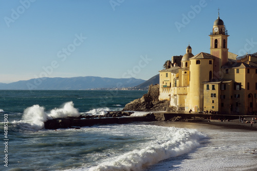 Stunning view of the picturesque town of Camogli with its church on the sea and the waves crashing on the dock.