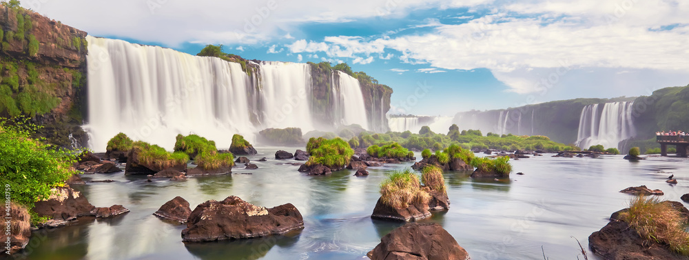 Iguazu waterfalls in Argentina, view from Devil's Mouth. Panoramic view of many majestic powerful water cascades with mist and clouds. Panoramic image of Iguazu valley with stones in water. - obrazy, fototapety, plakaty 
