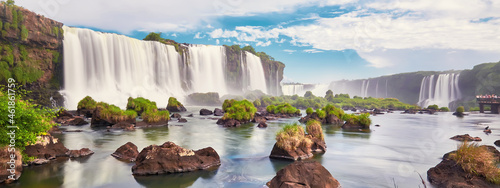 Iguazu waterfalls in Argentina, view from Devil's Mouth. Panoramic view of many majestic powerful water cascades with mist and clouds. Panoramic image of Iguazu valley with stones in water.