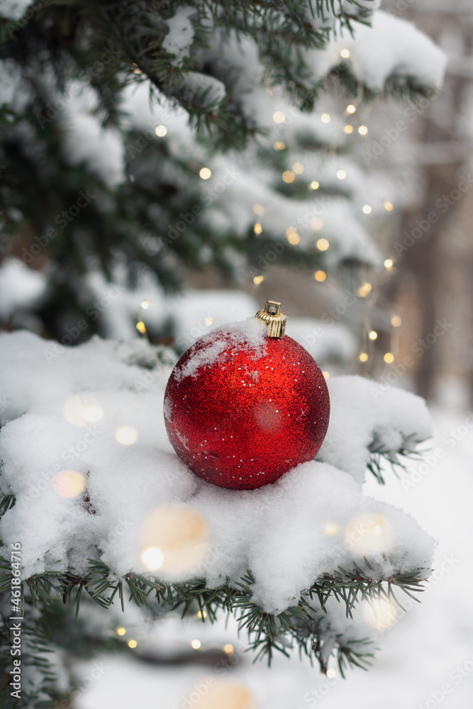 Shiny red Christmas bauble on the fir tree branch with snow and fairy lights. New Year winter holiday concept. Shiny red Christmas bauble on the fir tree branch with snow and fairy lights. New Year winter holiday concept.