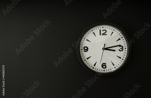 Clock hanging on the wall, with copy space on black background.