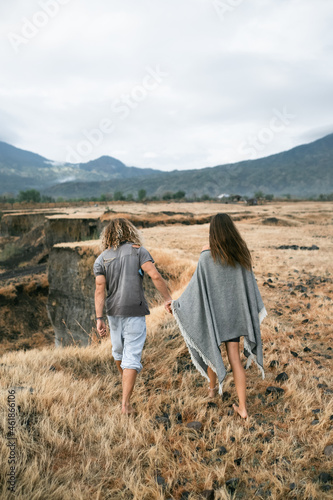 Man and woman in stylish clothes, look at the mountains and hold hands, autumn, back view.