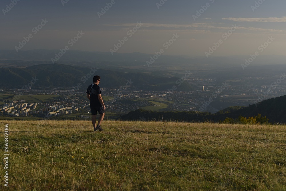 Fototapeta premium man walking up the hill above the city at sunset 