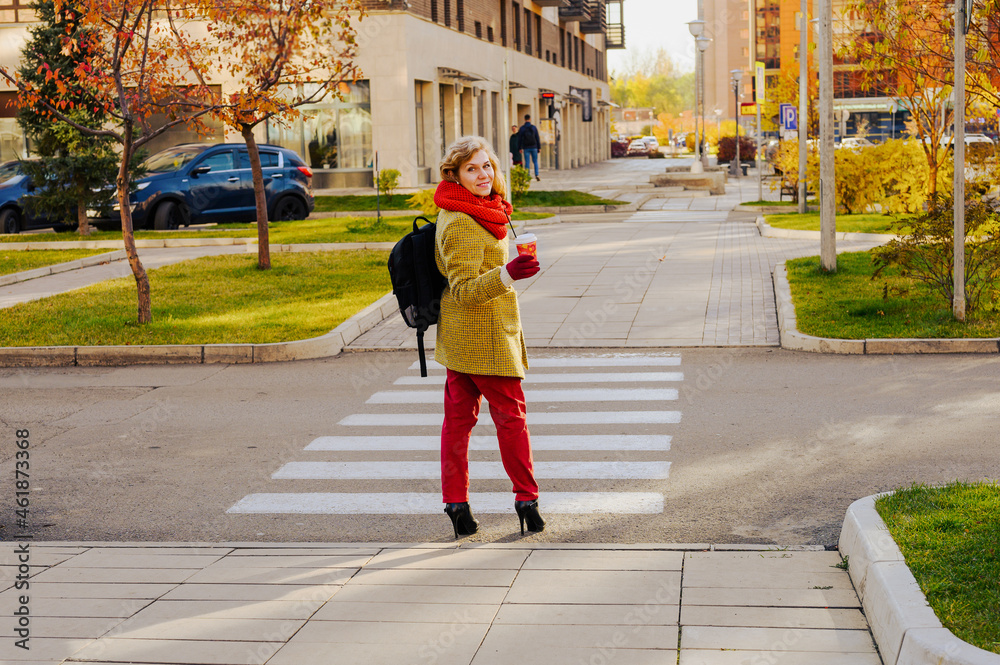 Woman with a cup of coffee about to cross the road on a zebra crossing in the city