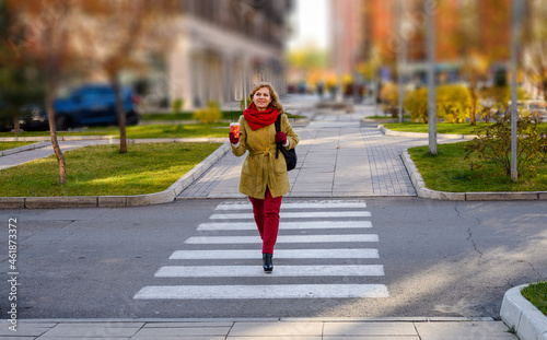 Woman with a cup of coffee crosses the road on a zebra crossing in the city