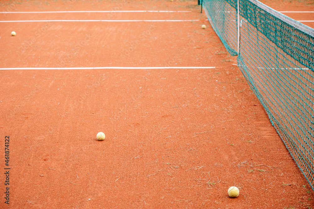 Empty clay tennis court. Tennis balls near net. White stripes. Dry grass.