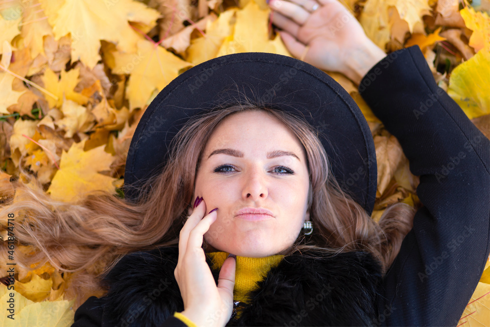 beautiful girl smile, young happy woman in black hat lying in orange leaves in autumn park. closeup portrait of stylish smiling lady in yellow clothes. fashion female fall outdoors