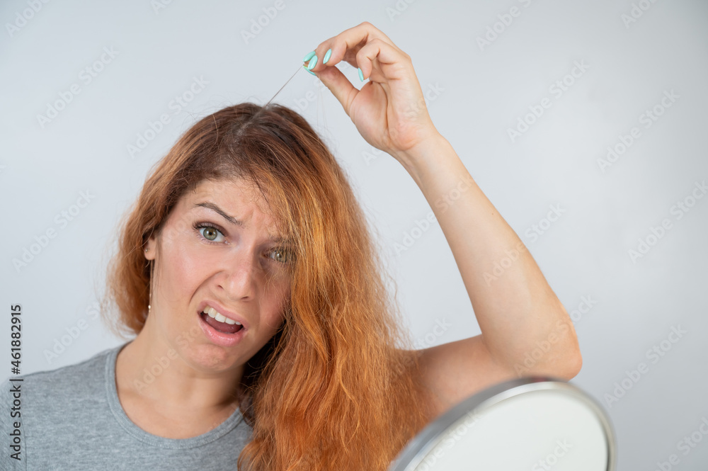Fototapeta premium Caucasian woman finds gray hair and removes it with tweezers. Signs of aging.