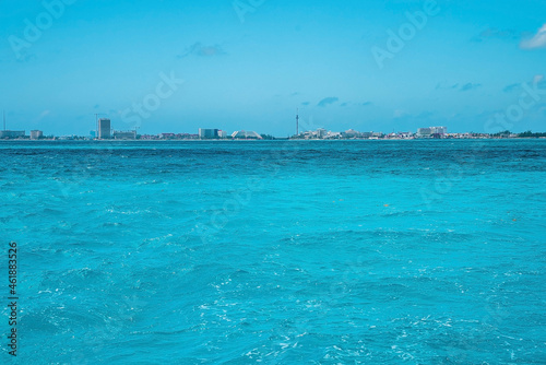 Beautiful scenic view of sea water surface with urban city buildings or hotels in the distant against cloudy sky