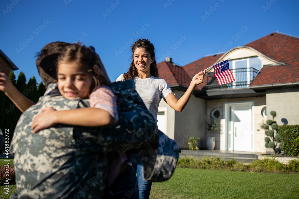 Happy reunion of soldier with his family outdoors in front of their house.