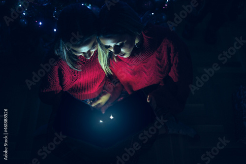 Cheerful woman opening magical Christmas gift box under tree at home