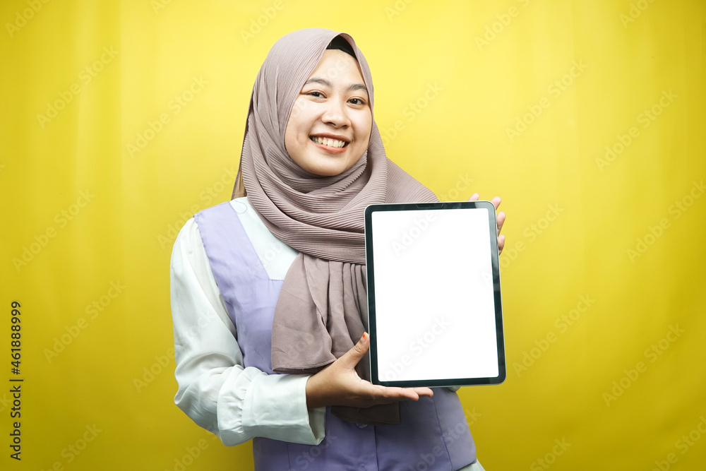 Beautiful young asian muslim woman smiling, excited and cheerful holding tablet with white/blank screen, promoting app, promoting product, presenting something, isolated on yellow background Beautiful young asian muslim woman smiling, excited and cheerful holding tablet with white/blank screen, promoting app, promoting product, presenting something, isolated on yellow background