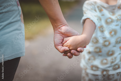 A mother holds her child's hand in concern while outdoors.