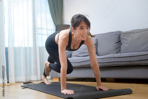 Happy young woman in sportswear is exercising in living room at home