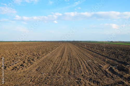 Freshly plowed field ready for seeding and planting in spring. Farmland. Empty plowed farm land prepared for the new crop. Agriculture. Brown black soil near village.