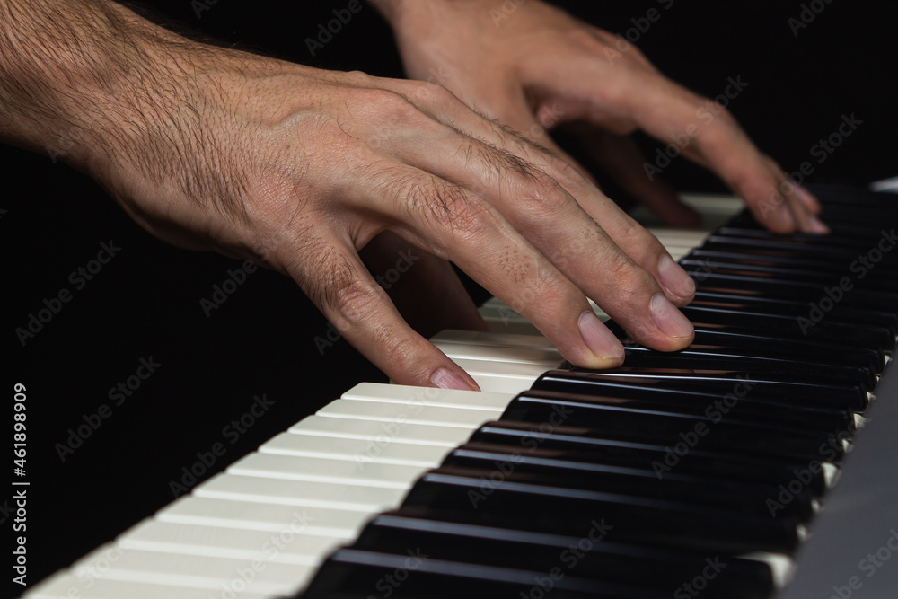 The hand plays the keyboard. Synthesizer keys on a black background. Musical instrument