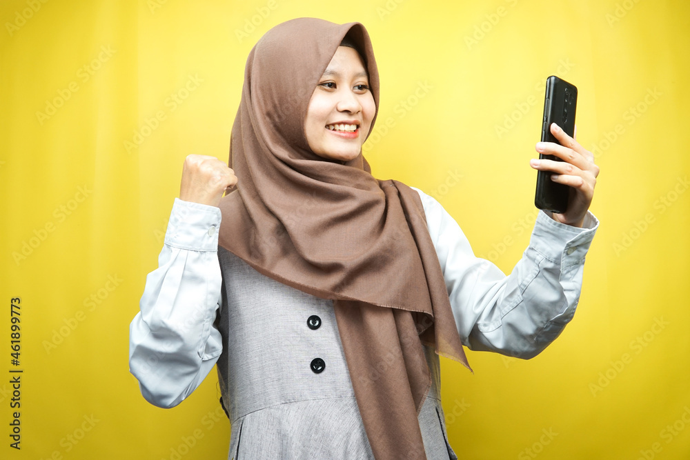 Beautiful young asian muslim woman smiling confident, enthusiastic and cheerful with hands holding smartphone, hands clenching, punching, victory, success, good work, isolated, advertising concept Beautiful young asian muslim woman smiling confident, enthusiastic and cheerful with hands holding smartphone, hands clenching, punching, victory, success, good work, isolated, advertising concept
