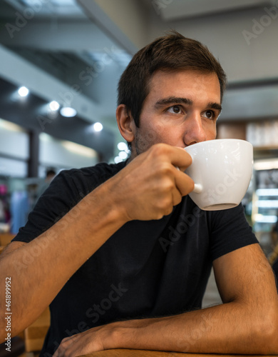 young hispanic man drinks coffee while looking away - coffee shop