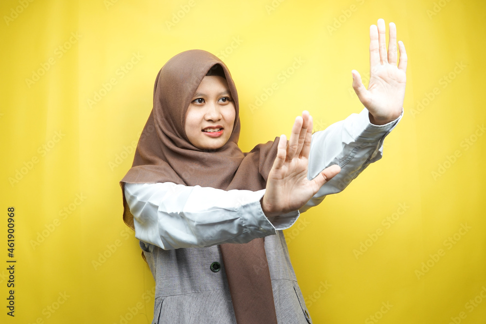 Beautiful asian young muslim woman with hand rejecting something, hand stopping something, disliking something in empty space, isolated on yellow background