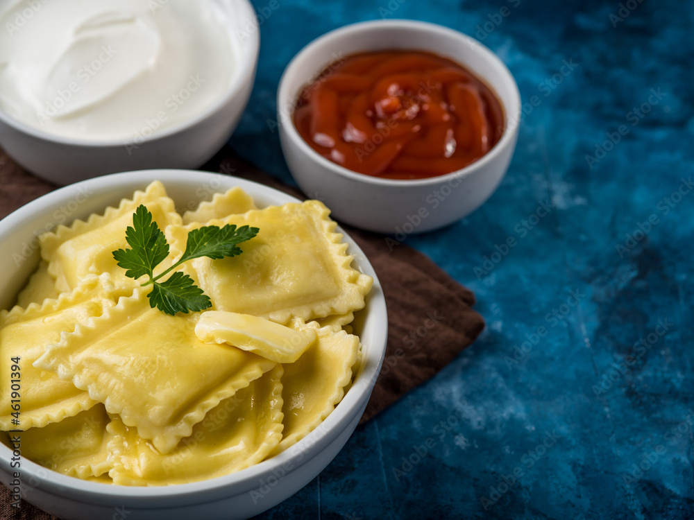 A portion of Italian ravioli, garnished with a mint leaf and two sauces - tomato and sour cream on a beautiful marble blue background. Restaurant, cafe, hotel, menu design. A portion of Italian ravioli, garnished with a mint leaf and two sauces - tomato and sour cream on a beautiful marble blue background. Restaurant, cafe, hotel, menu design.