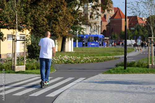 Dojżały mężczyzna jedzie na hulajnodze elektrycznej po ścieżce rowerowej.