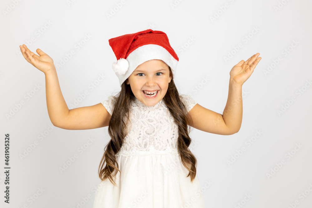 portrait of laughing, charming girl with long hair in white dress, wearing red Santa Claus hat with hands up, isolated on white background with copy space. portrait of laughing, charming girl with long hair in white dress, wearing red Santa Claus hat with hands up, isolated on white background with copy space.