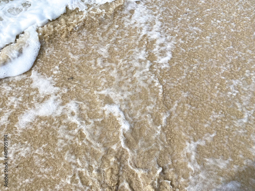 White sea wave foam crashing on clear wet sand on sea shore and tide pulling the water back