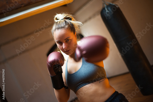 Gorgeous young sportswoman in boxing gloves. Attractive woman in sport clothes standing at gym in combative position, punching at camera. Sport, healthy lifestyle, boxing concept © KAMPUS