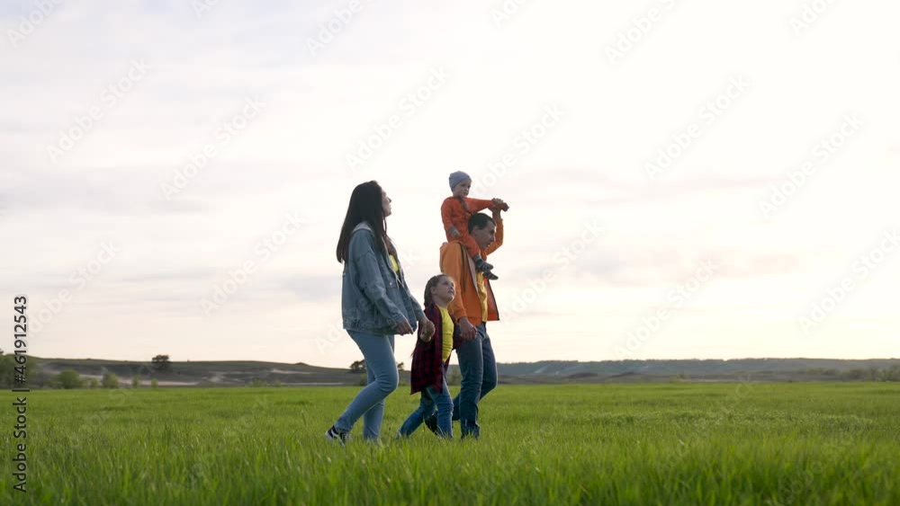 Happy family is walking on green grass. Mom dad and girl with toddler in park at sunset. Happy family walking in park at sunset. Mom dad girl and baby on green grass. Happy family concept at sunset Happy family is walking on green grass. Mom dad and girl with toddler in park at sunset. Happy family walking in park at sunset. Mom dad girl and baby on green grass. Happy family concept at sunset