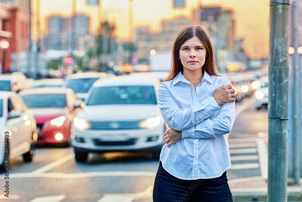 European woman in shirt stands on road near traffic.