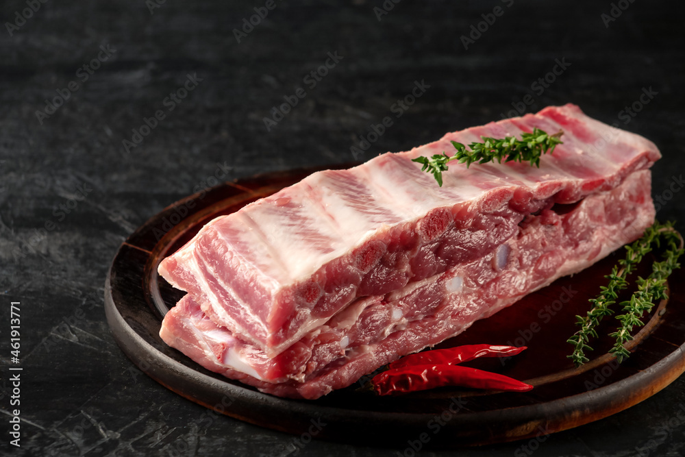 Raw pork ribs with spices and thyme on a dark wooden background