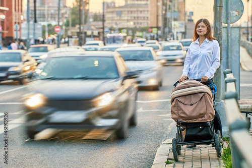 European woman walks with baby in buggy near traffic.