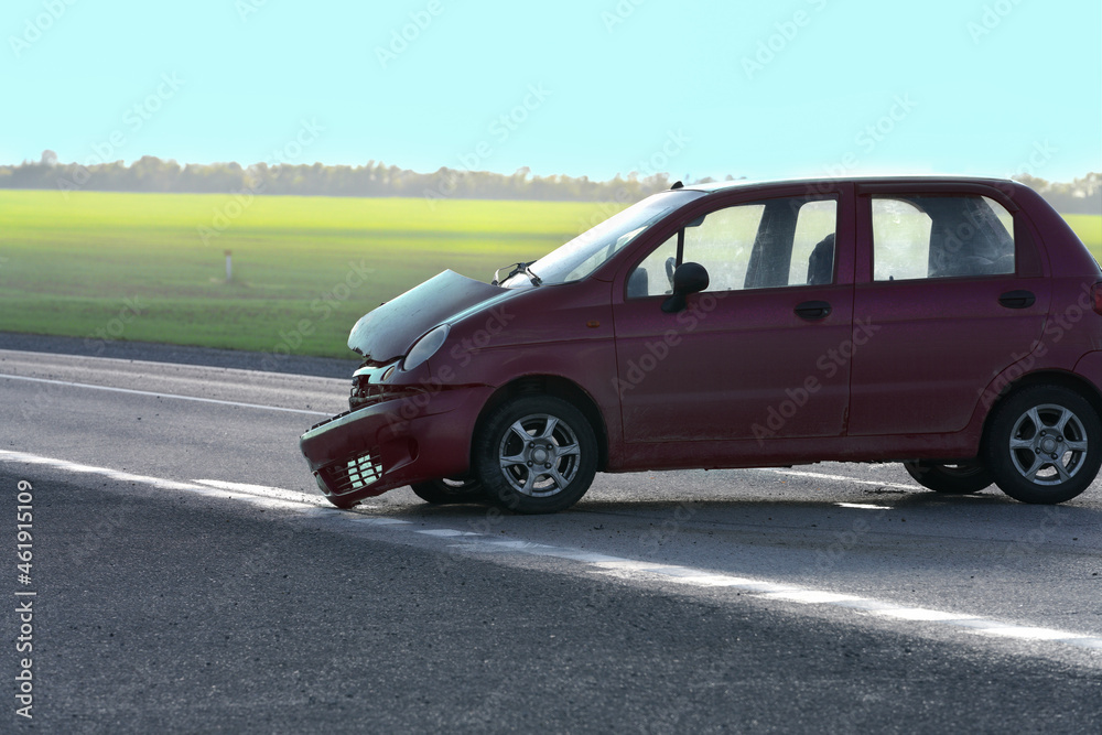 An accident on the road. A car with a broken hood and a torn bumper is standing across the road. Copy space.