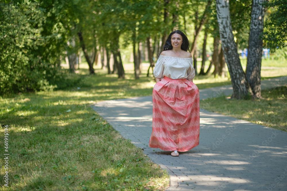 Middle-aged attractive woman with dark hair, enjoying nature in the forest. Walking among the trees in the sunlight. self-sufficient confident woman Middle-aged attractive woman with dark hair, enjoying nature in the forest. Walking among the trees in the sunlight. self-sufficient confident woman
