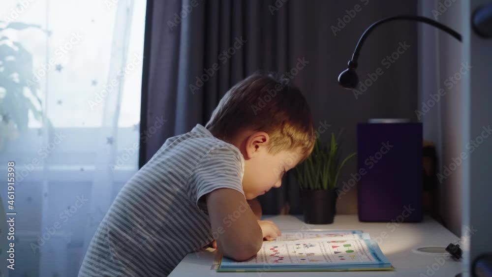 Little boy doing homework at home. kid reading a book at the table by the light of lamp. High quality FullHD footage Little boy doing homework at home. kid reading a book at the table by the light of lamp. High quality FullHD footage