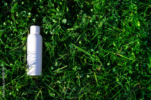in the green grass lies a white bottle with cosmetics. autumn aroma of morning frosty freshness.