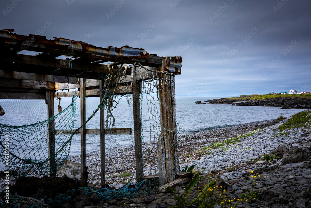 Abandoned fisherman's net shed on a gray, stony beach. Cloudy sky. 
