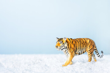 Tiger symbol of the Chinese new year 2022. Figurine of tiger in snow on blue background. Christmas greeting card. Banner, copy space.